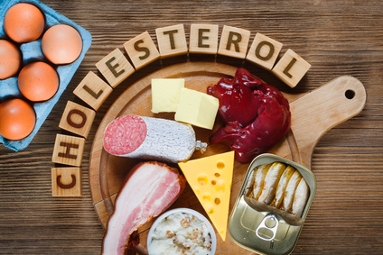 Na drewnianej desce znajduje się ser, mięsko, ryby. Wyżej z drewnianych klocków został ułożony napis "Cholesterol"