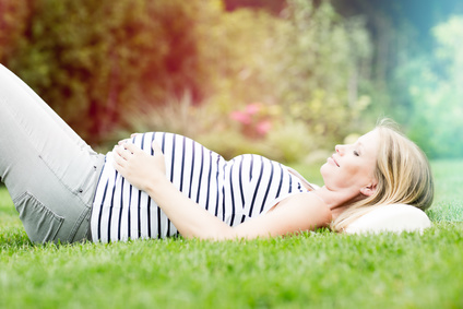 Kobieta w ciąży leżąca na trawie.